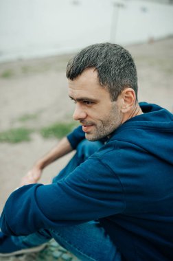 Koyu renkli ama deniz kenarında kısmen gri kapüşonlu genç adamın portresi. Koyu uzun erkek kirpikleri. seçici odak