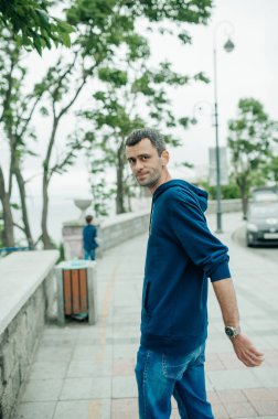 Şehir caddesinde yürüyen orta yaşlı bir adam. Koyu renkli ama deniz kenarında kısmen gri kapüşonlu genç adamın portresi. şehir tarzı içerik. seçici odak