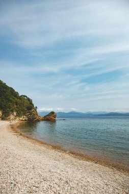 Yaz masmavi deniz manzarası. Etrafında resifler, kayalar ve yeşil tepeler olan saydam bir deniz. Japon denizi. Rusya 'da Primorsky Krai, Putyatina Adası