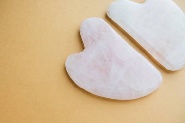 Temiz bir bej arka planda gül kuvarstan yapılmış yüz masajı kazıyıcısı. Kozmetik çizimi. Evde yüz bakımı. seçici odak