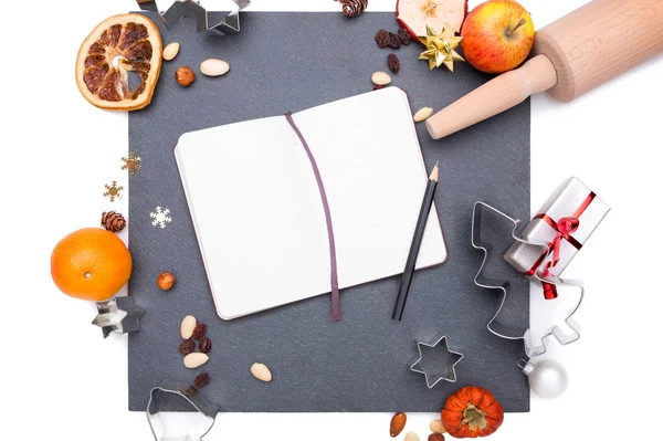 Placa de pizarra con un cuaderno y cosas de Navidad a su alrededor . —  Fotos de Stock