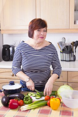 Orta yaşlı ev hanımı sebze pişiriyor. 