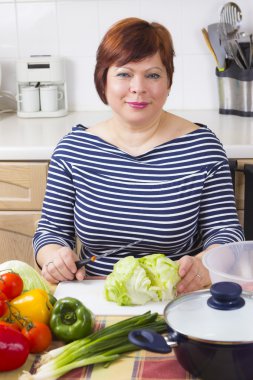 Orta yaşlı ev hanımı sebze pişiriyor. 