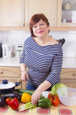 Orta yaşlı ev hanımı sebze pişiriyor.