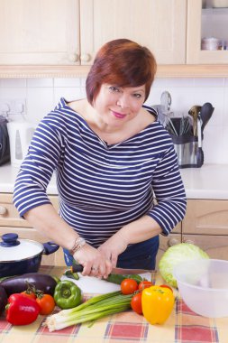 Orta yaşlı ev hanımı sebze pişiriyor.