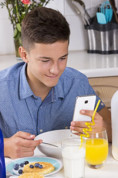 Pojke med telefonen äter frukost i köket — Stockfoto