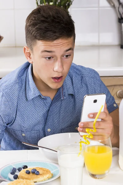 Boy with phone having breakfast in kitchen — Stock Photo, Image