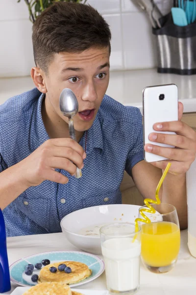 Boy with phone having breakfast in kitchen — Stock Photo, Image