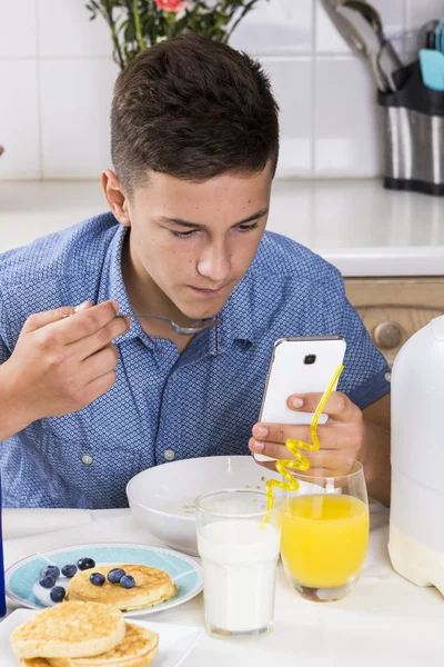 Pojke med telefonen äter frukost i köket — Stockfoto