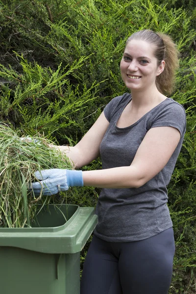 Девушка с травой рядом с зеленым мусорным баком — стоковое фото