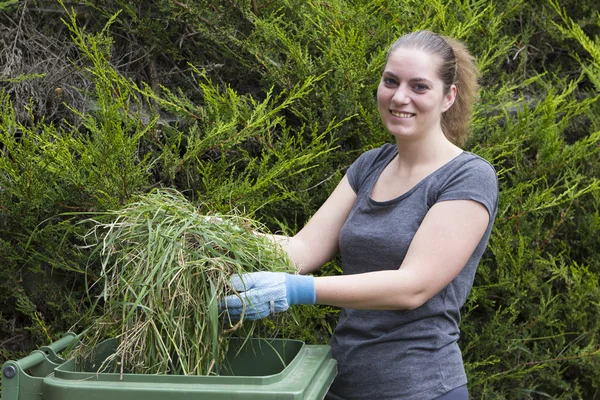 Девушка с травой рядом с зеленым мусорным баком — стоковое фото