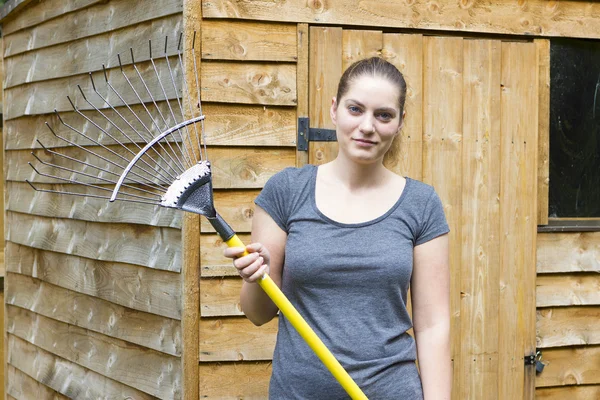 Mujer joven rastrillando hierba en el jardín — Foto de Stock