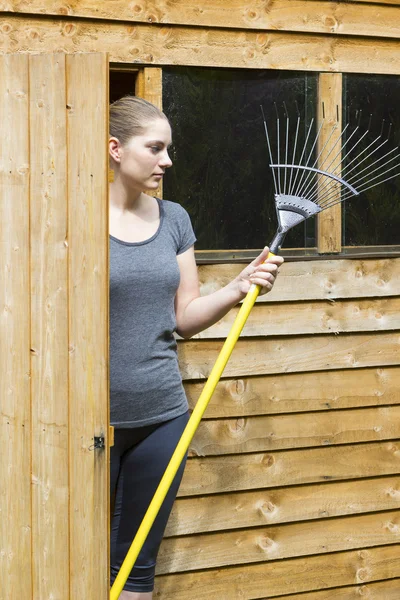 Jovem mulher raking grama no jardim — Fotografia de Stock