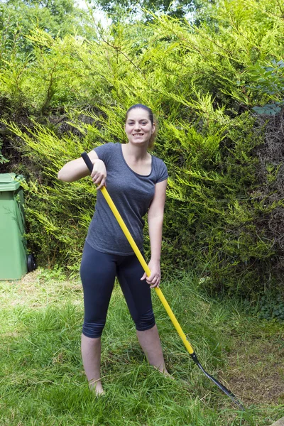 Jonge vrouw harken gras in de tuin — Stockfoto