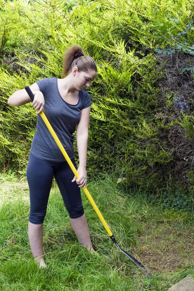 Jovem mulher raking grama no jardim — Fotografia de Stock