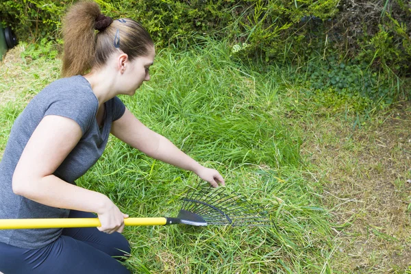 Ung kvinna krattar gräs i trädgården — Stockfoto