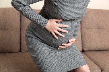 Hamile kadın, alt karın masajı yaptırıyor. İçeride, koltukta oturuyor. Hamilelik Sorunları Konsepti. Annelik sağlık hizmetleri.