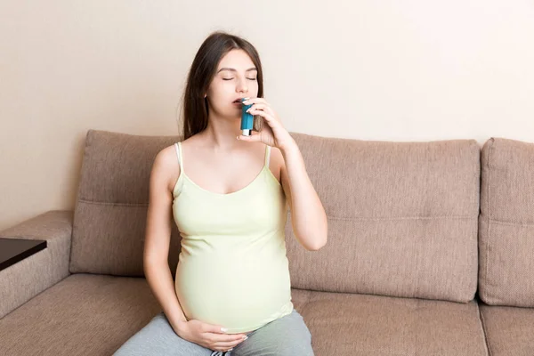 喘息吸入器を使う妊婦は自宅のソファで健康であることを攻撃中 健康的な千年紀医療の概念 — ストック写真