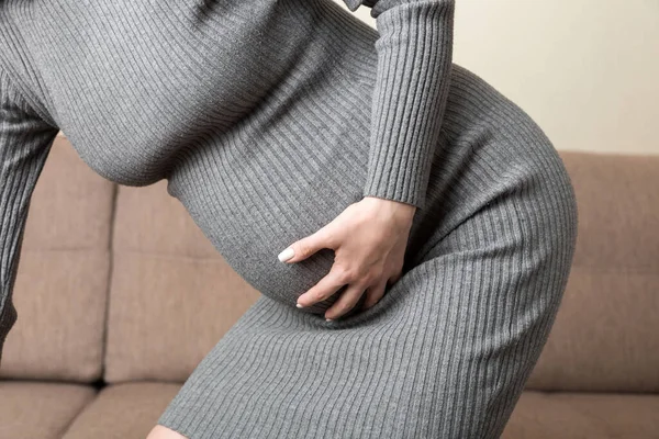 有按摩下腹的孕妇坐在索法室内 怀孕问题概念 产妇保健 — 图库照片