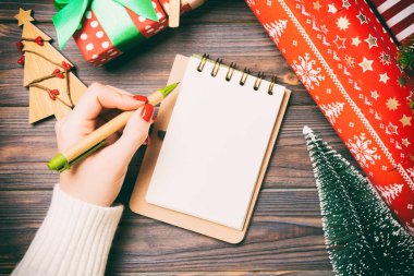 Ahşap Noel arka planında bir not defterine kadın el yazısının üst görüntüsü. Firavun ağacı ve şenlikli süsler. Dilek listesi. Yeni yıl konsepti.