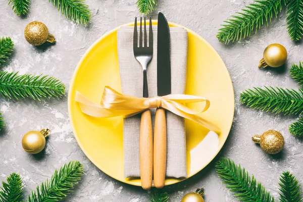 Top view of New Year dinner on festive cement background. Composition of plate, fork, knife, fir tree and decorations. Merry Christmas concept.