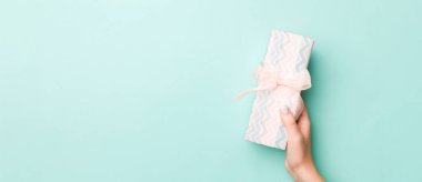 Kadın elleri renkli kağıda sarılı Noel veya diğer tatil hediyelerini verir. Hediye kutusu, hediye süslemesi mavi masada, üst görünümde kopya alanı.