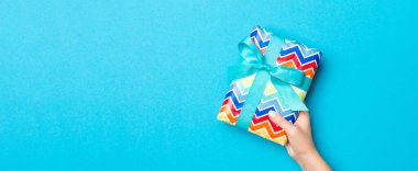 Mavi masa arkasında renkli kurdeleli hediye paketi olan kadın kolları, üst görünüm ve sizin için kopyalama alanı.