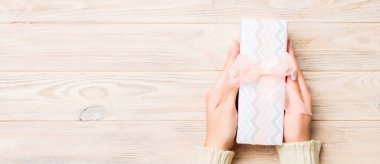 Kadın elleri renkli kağıda sarılı Noel veya diğer tatil hediyelerini verir. Hediye kutusu, hediye süsü sarı kırsal ahşap masa, fotokopi alanı olan üst manzara..