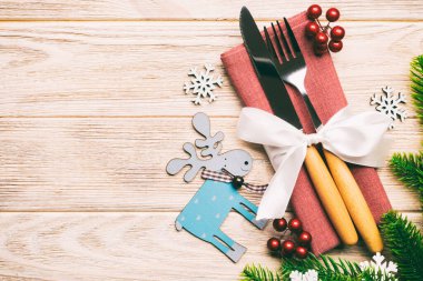 Tahta arka plandaki tatil eşyalarının üst görüntüsü. Utensiller peçeteye kurdele ile bağlanmış. Noel süsleri ve fotokopi alanı olan ren geyikleri. Yeni yıl yemeği konsepti.