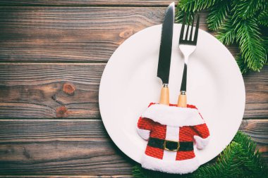 Ahşap arka planda Noel Baba kıyafetleriyle süslenmiş tabak ve çatal bıçaklardan oluşan tatil kompozisyonu. Tasarımınız için boş yeri olan Noel süslemelerinin en üst görüntüsü. Eğlence zamanı konsepti.