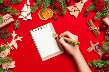 Kadın elinin rengarenk arka planda notlar aldığına dair üst görünüm. Yeni yıl süslemeleri ve oyuncakları. Noel zamanı konsepti.