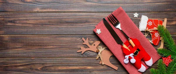 Banner top view of holiday objects on wooden background. Utensils tied up with ribbon on napkin. Christmas decorations and reindeer with copy space. New year dinner concept.