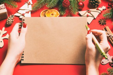 Kadın elinin kırmızı arka planda notlar alırken üst görüntüsü. Yeni yıl süslemeleri ve oyuncakları. Noel zamanı konsepti.