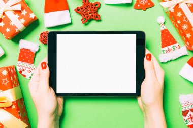 Elinde tabletle Noel süslemelerinden yapılmış yeşil arka planda gezen kadının üst görüntüsü. Yeni yıl tatili konsepti. Model.