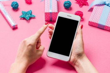 Neşeli pembe arka planda kadın elinin telefonunun üst görüntüsü. Noel süsleri. Yeni yıl tatili. Model.