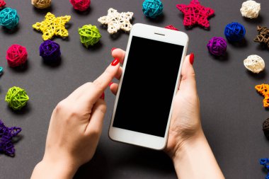Bayramlık siyah arka planda kadın elinin telefonunun üst görüntüsü. Noel süsleri. Yeni yıl tatili. Model.