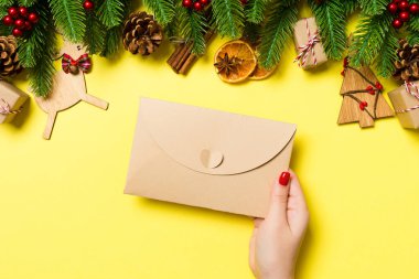 Bayram süslemelerinden yapılmış sarı arka planda bir zarf tutan kadının üst görüntüsü. Noel zamanı konsepti.