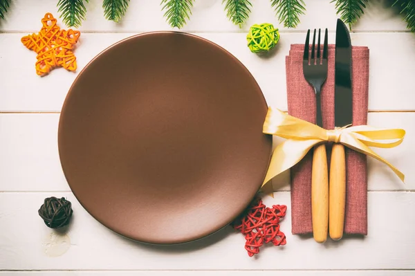 Top view of New Year dinner on festive wooden background. Composition of plate, fork, knife, fir tree and decorations. Merry Christmas concept.