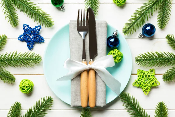 Top view of New Year dinner on festive wooden background. Composition of plate, fork, knife, fir tree and decorations. Merry Christmas concept.