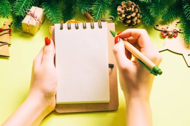 Kadın elinin sarı arka planda notlar alırken üst görüntüsü. Yeni yıl süslemeleri ve oyuncakları. Noel zamanı konsepti.