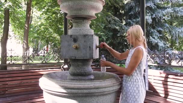 Genç bir kadın kaynağından su içiyor. Dışarıda maden suyu olan pompa. — Stok video