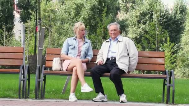 Καυκάσιο ηλικιωμένο ζευγάρι με καθημερινά ρούχα κάθεται στον πάγκο και μιλάει με τον Γούμαν στο πάρκο — Αρχείο Βίντεο