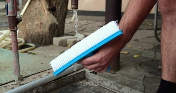 Un homme nettoie une brosse blanche sous l'eau dans la rue — Video