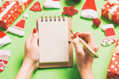 Kadın elinin yeşil arka planda notlar alırken üst görüntüsü. Yeni yıl süslemeleri ve oyuncakları. Noel zamanı konsepti.