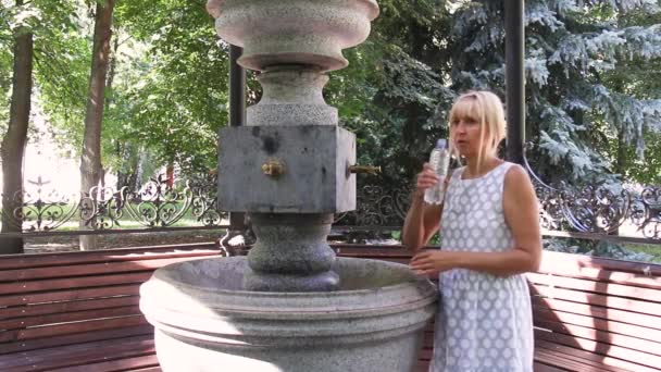 Młoda kobieta pijąca wodę w butelce ze źródła. pompa z wodą mineralną na zewnątrz — Wideo stockowe