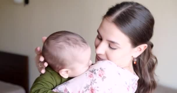 Mamá beso recién nacido bebé hijo sostiene en sus brazos jugando en el hogar. madre día, feliz concepto de familia — Vídeo de stock