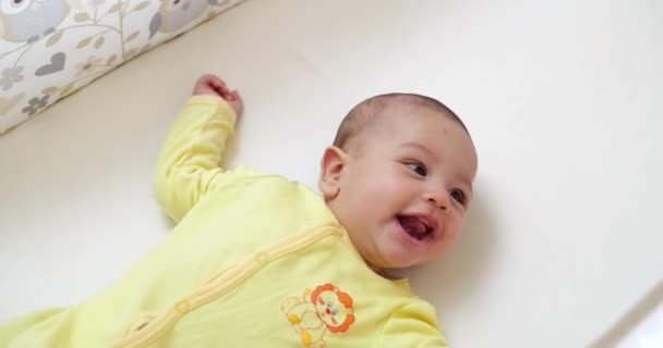 En trevlig liten kaukasisk nyfödd bebis är rolig leende, liggande vid barnsäng. Vackert leende Baby på sängen hemma — Stockvideo