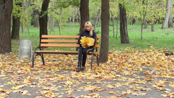Mulher loira senta-se em um banco no parque. Outono em um dia de sol — Vídeo de Stock