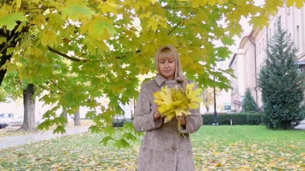 Belle femme aux feuilles jaunes près d'un bel arbre se réjouit du bouquet recueilli dans le parc — Video