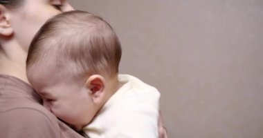 Anne, ağlayan bir bebeği kollarında rahatlatır ve kucaklar. Annenin kollarındaki bebek kameraya bakıyor. Annelik kavramı